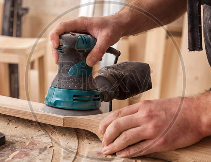 Close Up Of An Young Man Builder Carpenter Equals Polishes Wooden Board With A  Random Orbit Sander  In The Workshop