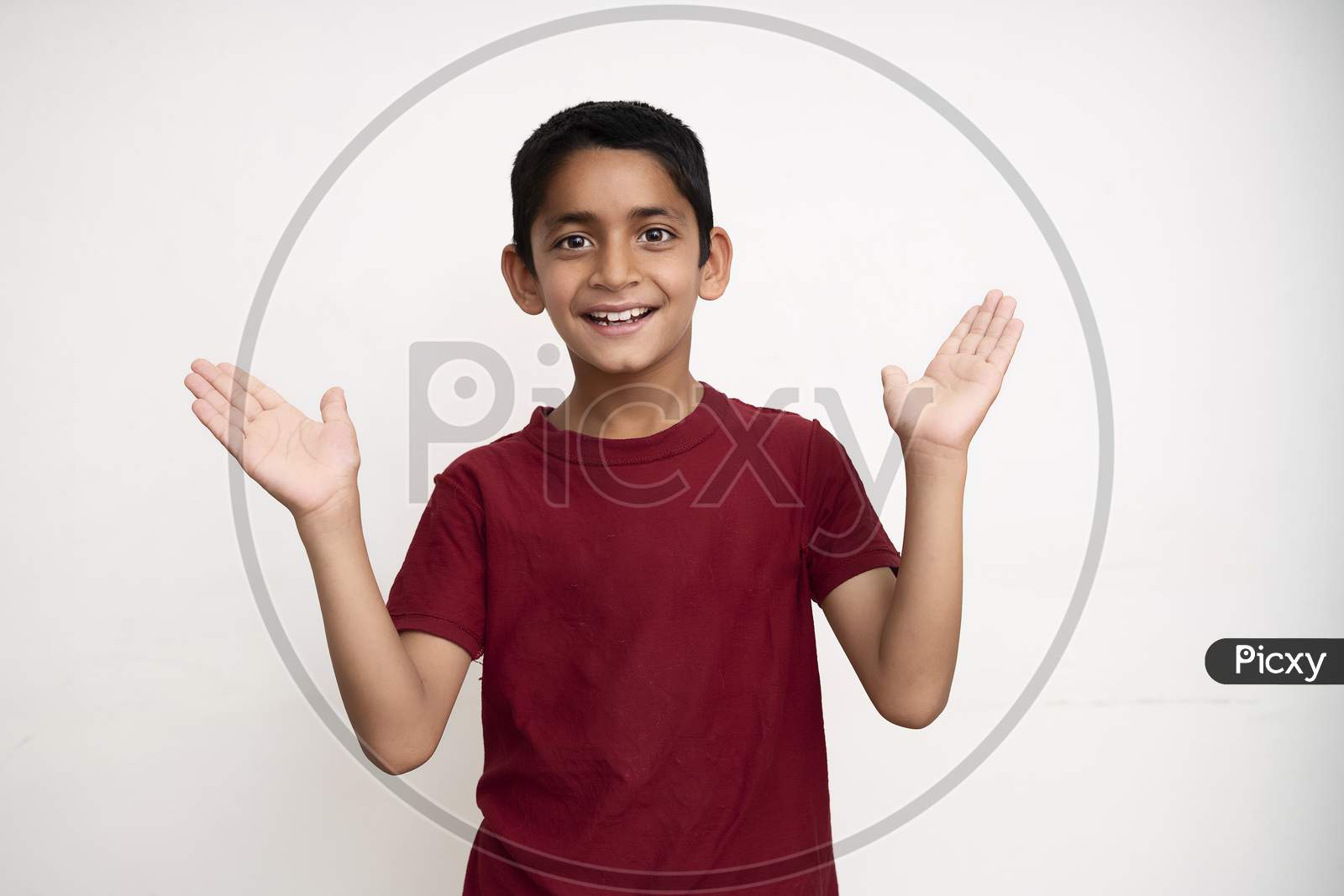 Young Indian Kid Acting Happy With His Arms Spread While Standing On A White Wall With Copy Space. Education And Fun Concept.