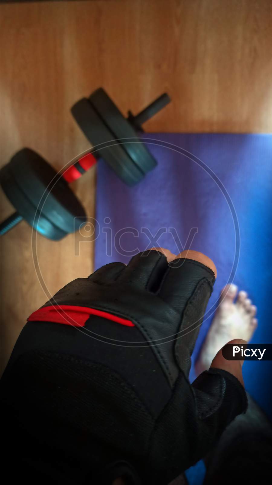 Work Out At Home Concept Showing Top View Of Weight Lifting Hand Glove With A Man Standing On Blue Neoprene Mat Next To A Hand Lift Dumbbell. Sports Concept During Epidemics, Pandemic, New Normal
