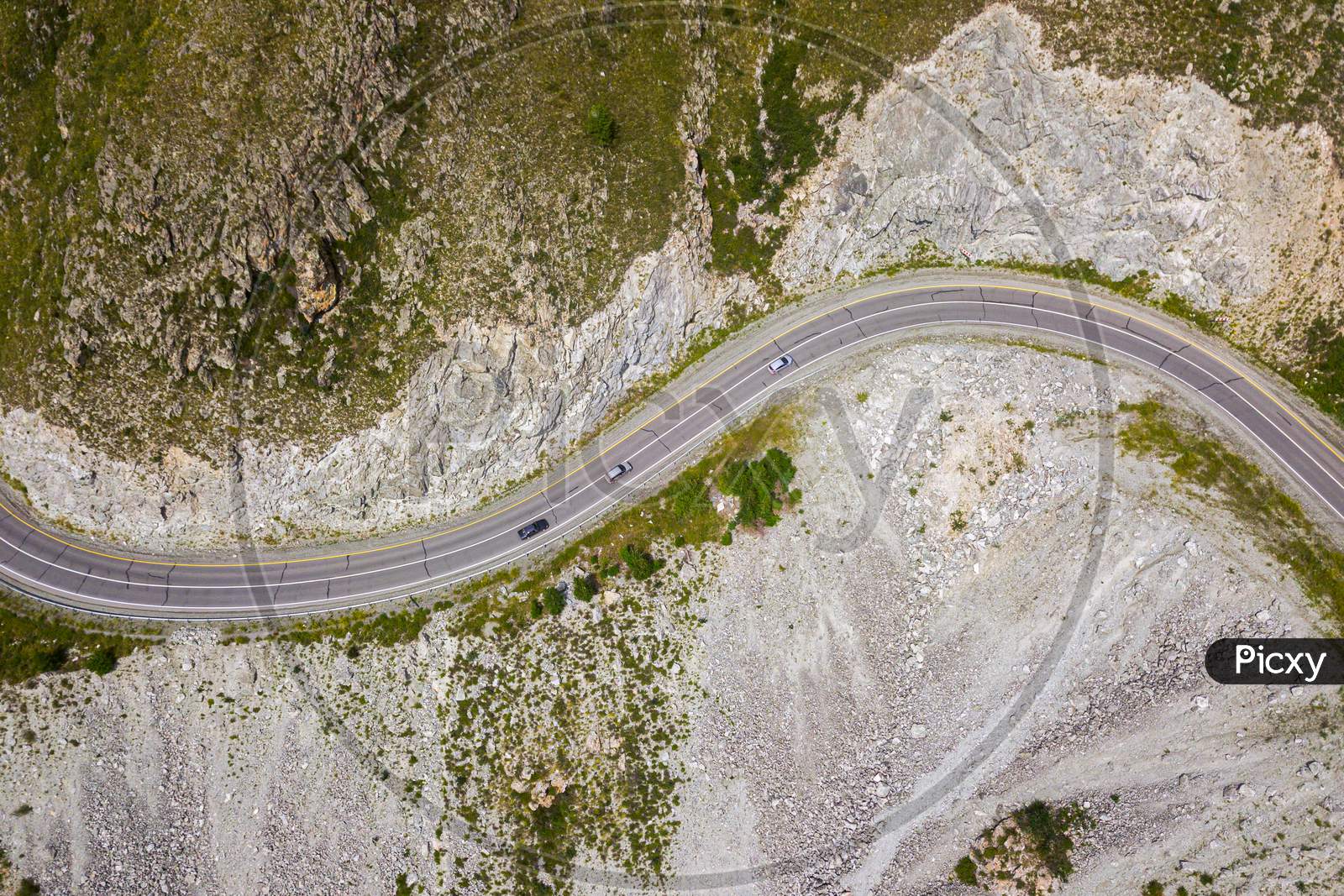 Highway Through The Mountains, High Mountains And A Green Forest On A Warm Summer Day On Each Side. Highway In The Mountains Aerial View