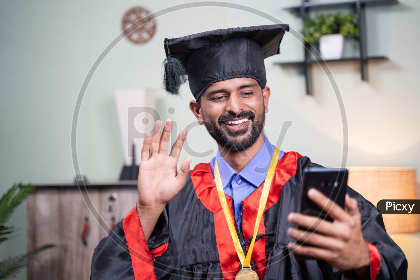 Student Attending His Online Video Graduation Celebration From Mobile Phone In Graduation Dress - Concept Of Virtual Celebrations, New Normal During Coronavirus Or Covid-19 Pandemic