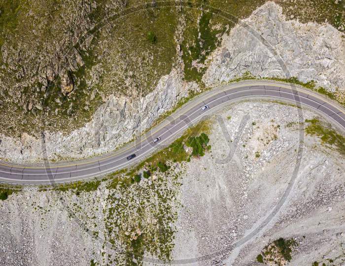 Highway Through The Mountains, High Mountains And A Green Forest On A Warm Summer Day On Each Side. Highway In The Mountains Aerial View