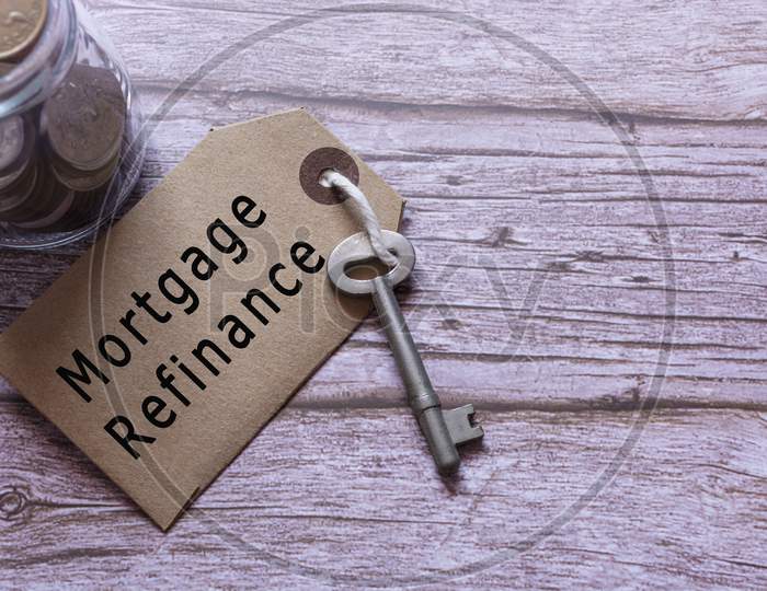Text On Brown Tag With Key And Blurred Jar Full Of Coins On Wooden Table - Mortgage Refinance