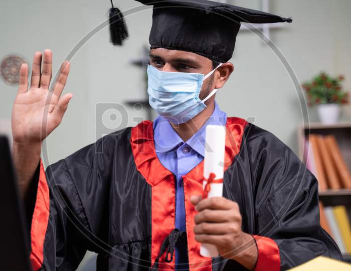 Student With Medical Face Mask Attending Virtual Video Graduation Celebration From Home On Laptop - Concept Of Healthcare,Safety And New Normal Lifestyle During Coronavirus Covid-19 Pandemic.