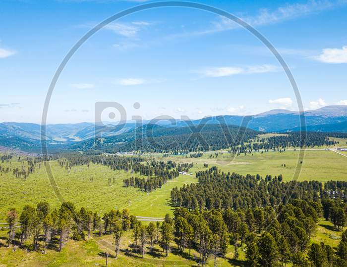 Helicopter Drone Shot. A View From Above Of  A Green Forest And A Large Field On A Warm, Sunny Summer Day.