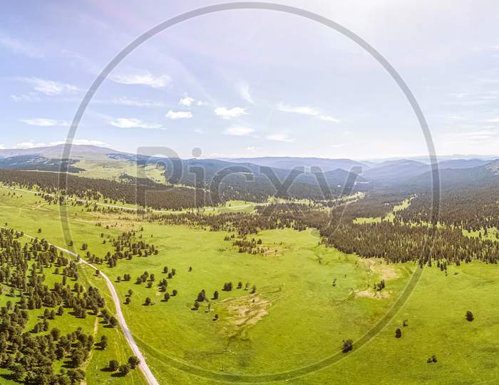 Panorama Of The Mountains  In Altai On A Summer Clear Day. A Landscape View Of Beautiful Fresh Green Field   And  Altai Mountain Background.  Panoramic View Of Beautiful Green Field