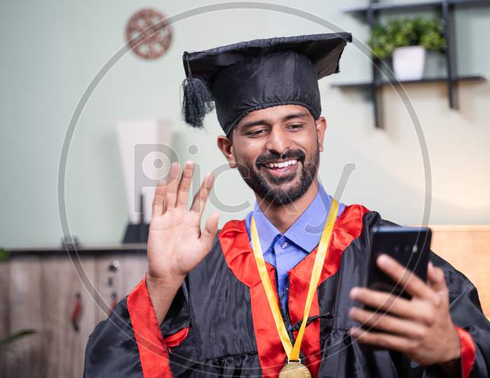 Student Attending His Online Video Graduation Celebration From Mobile Phone In Graduation Dress - Concept Of Virtual Celebrations, New Normal During Coronavirus Or Covid-19 Pandemic