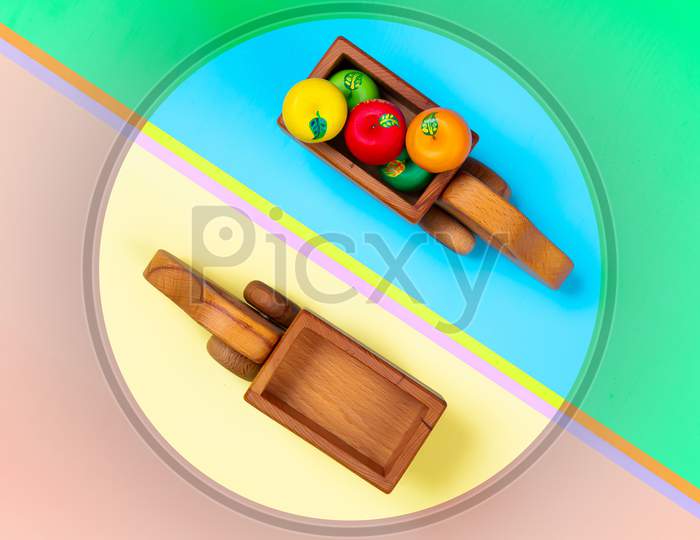 Minimalistic Flat Lay With A Wooden Toys Trucks With Apples On An Isolated Multicolored Vibrant Geometric Background. Toy For Entertaining Children And Parents