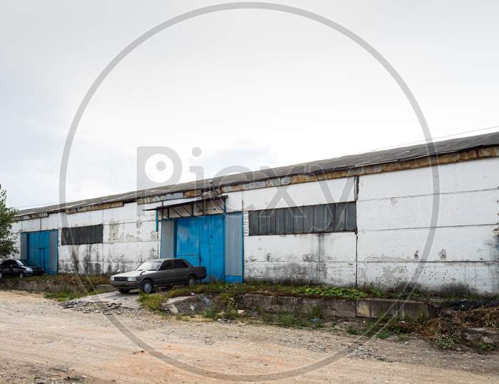 Facade On Large Industrial Building Made Of Metal White And Blue Panels. Industrial Concept Of Transportation, Loading And Storage Of Goods. The Car Is In The Loading Area