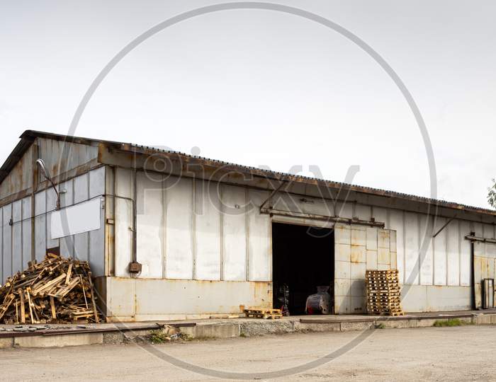 A Large Metal Industrial Warehouse For Storing Goods, Next To It Are Wooden Pallets For Storing Goods. Industrial Concept Of Transportation, Loading And Storage Of Goods