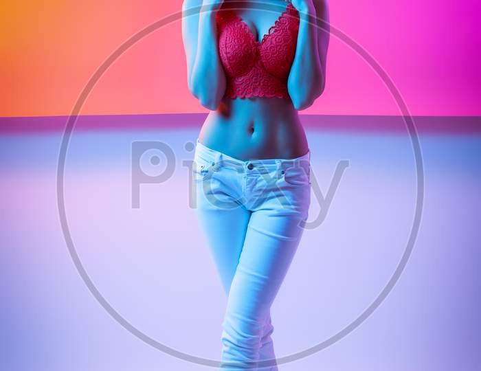 Attractive  Long-Haired Girl, Stylish Fashion. Design Art Concept. Creative Colorful Bright Neon Portrait . Beautiful Girl In Lingerie And Jeans Posing. Cinematic Night Portrait Of Woman In  Neon.