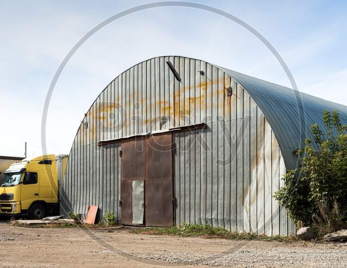 Facade Of A Gray Metal Warehouse, Commercial Building For Storage Of Goods. The Concept Of Storage Of Goods By Importers, Exporters, Wholesalers, Transport Enterprises, Customs
