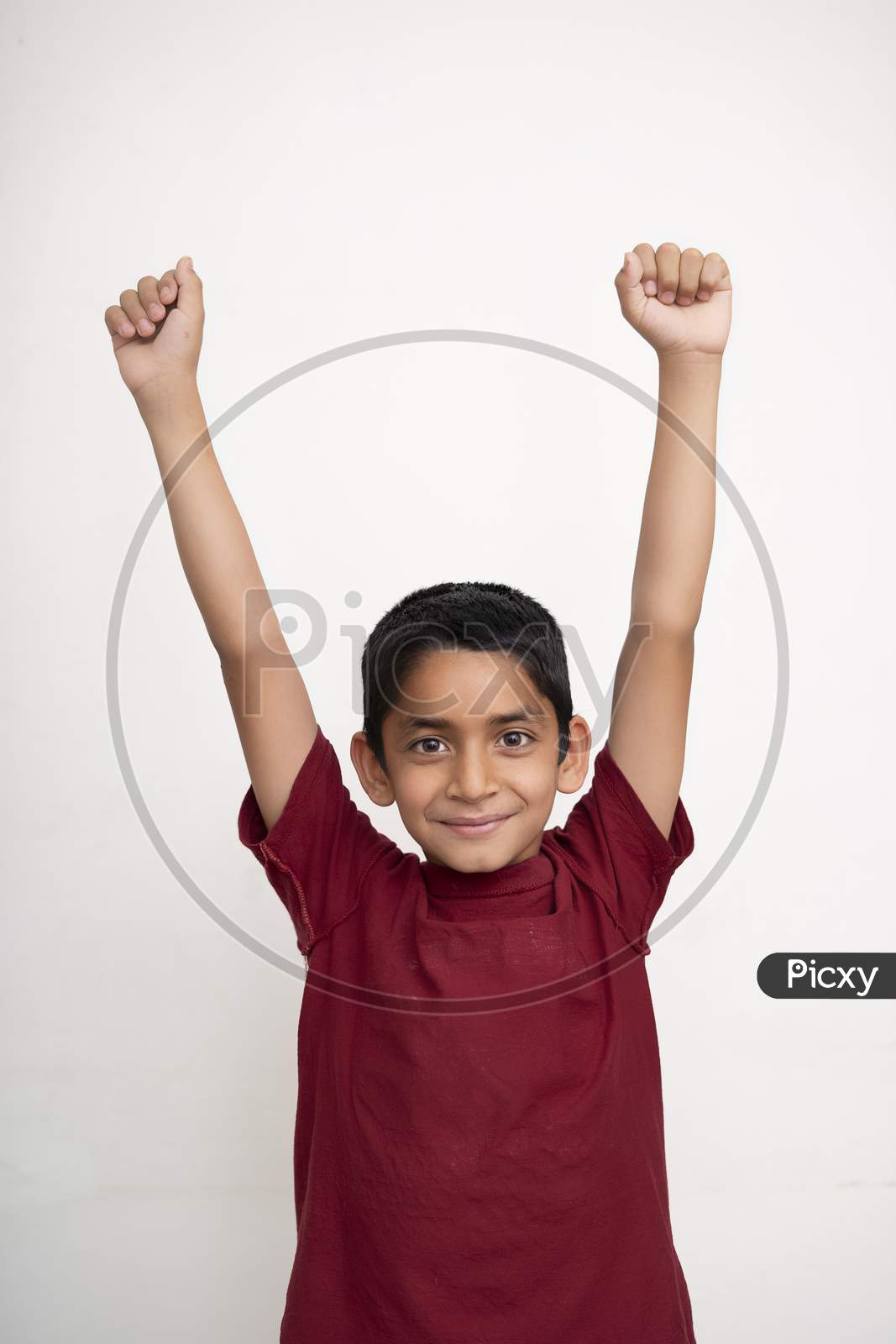 Young Indian Kid Showing Joy Expression With His Arms In The Air Standing On A White Isolated Background