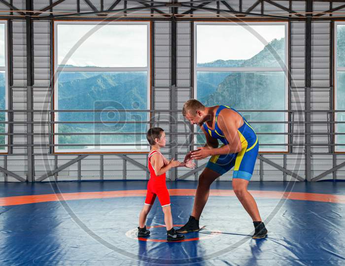 An Adult Male Wrestler Coach Teaches The Basics Of Wrestling And Sets Up A Little Boy To Compete. The Concept Of Child Power And Martial Arts Training. Teaching Children Greco-Roman Wrestling
