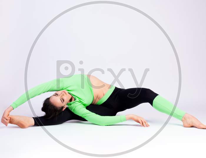 Slim Young Woman Doing Yoga Practice, Doing The Splits On A White Isolated Background. The Concept Of A Healthy Lifestyle And A Natural Balance For Women