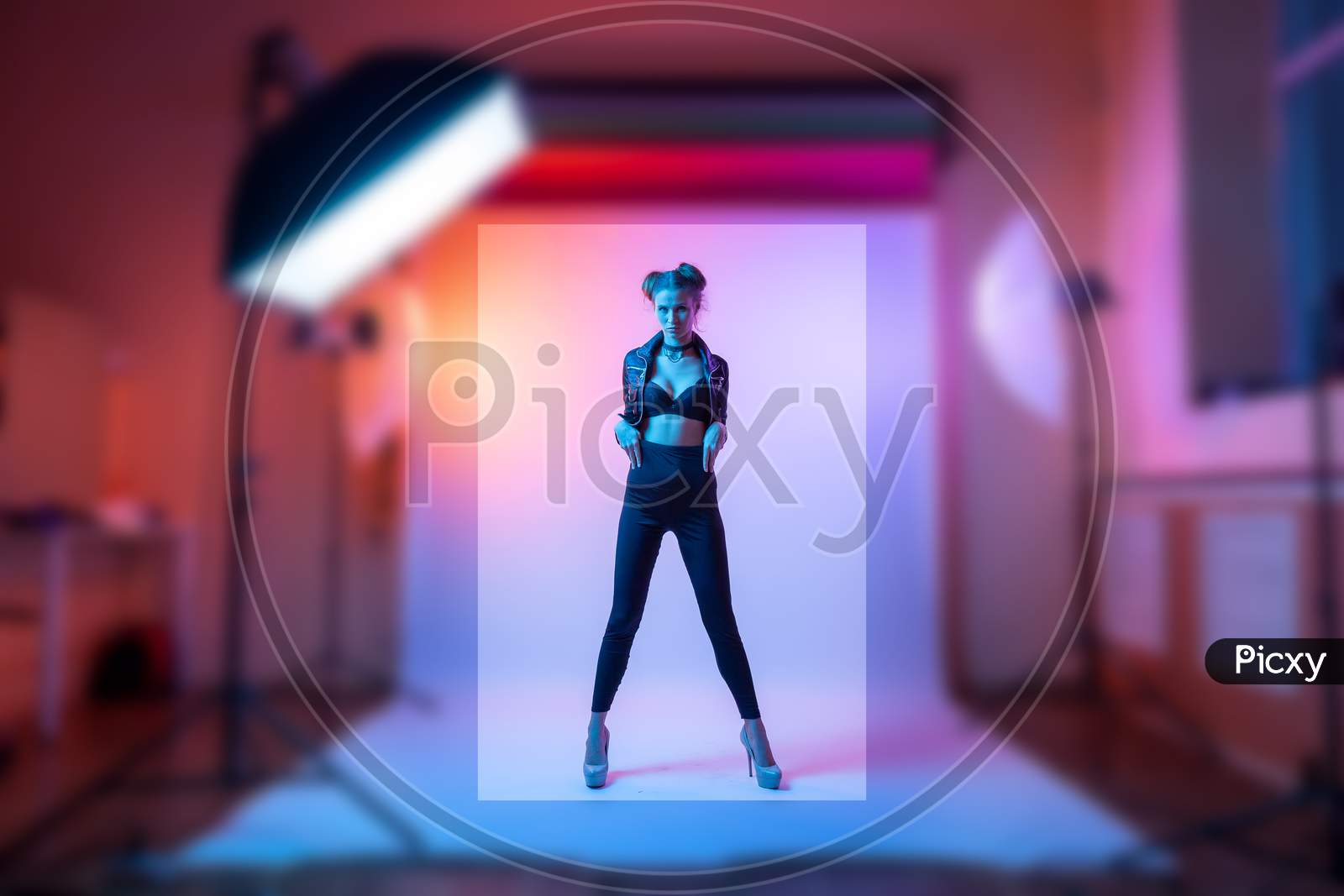 Photographing Clothes For A Catalog On A Stylish Thin Woman In A Photo Studio With Plain Colors And Bright Pink Neon Lighting. Fashion Shooting Concept For A Clothing Store.