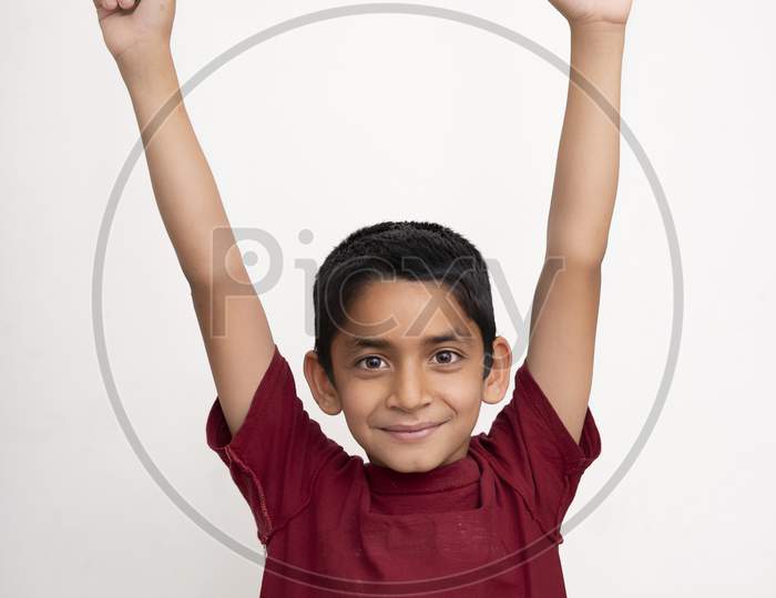 Young Indian Kid Showing Joy Expression With His Arms In The Air Standing On A White Isolated Background