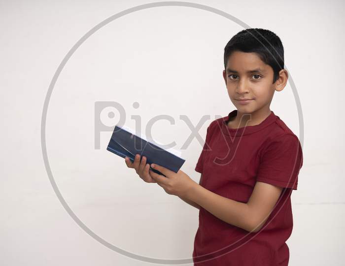 Young Indian Kid Standing On A White Isolated Background With A Book In His Hands. Education And Fun Concept.