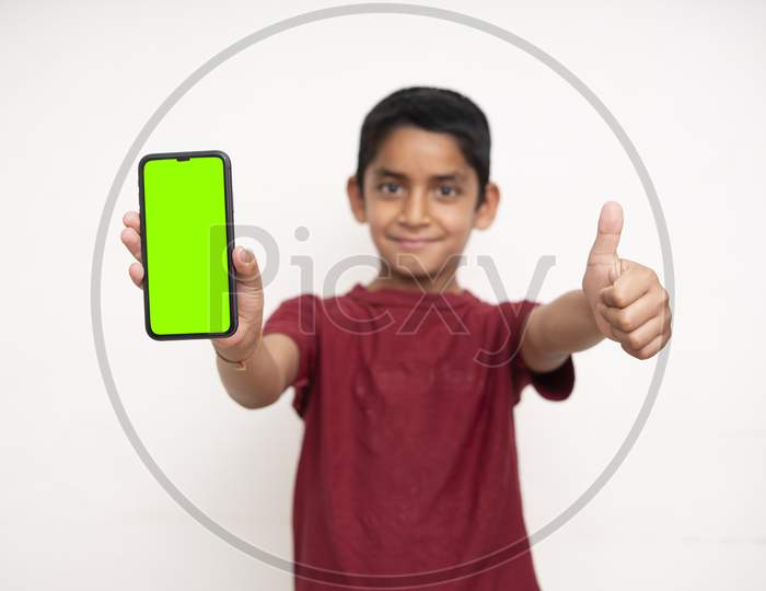 Young Indian Kid Holding A Phone In His Hands With A Green Screen Standing On A White Isolated Background With Copy Space.