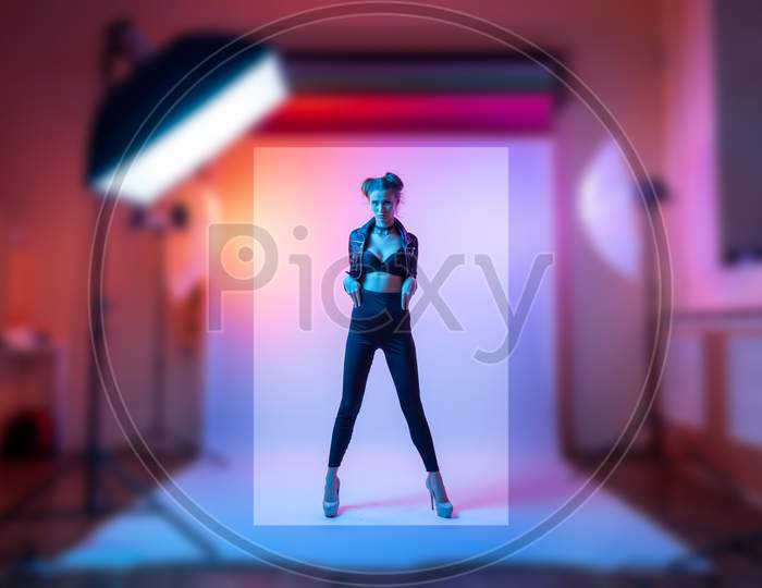 Photographing Clothes For A Catalog On A Stylish Thin Woman In A Photo Studio With Plain Colors And Bright Pink Neon Lighting. Fashion Shooting Concept For A Clothing Store.
