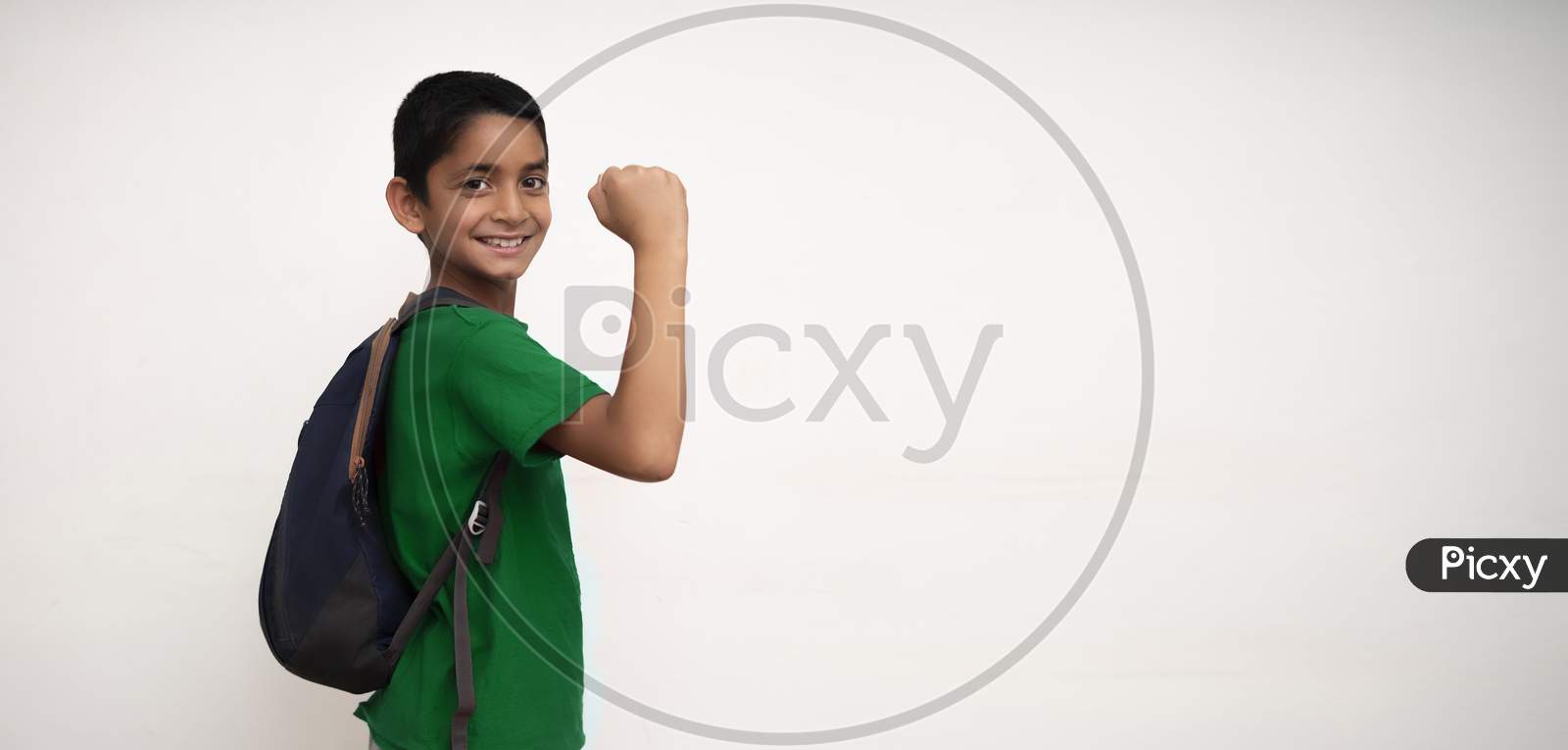 Banner Image Of An Indian Happy Kid Going To School With His Bag On His Back And Showing His Arms On A White Wall With Copy Space.