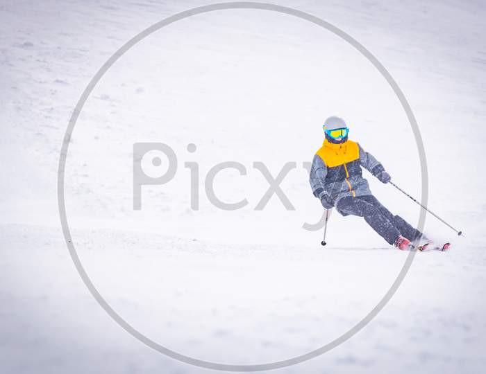 Low Angle Front View Male Person Alone Skiing Downhill In White Snowy Background. Bad Visibility And Solo Adventure In Mountains