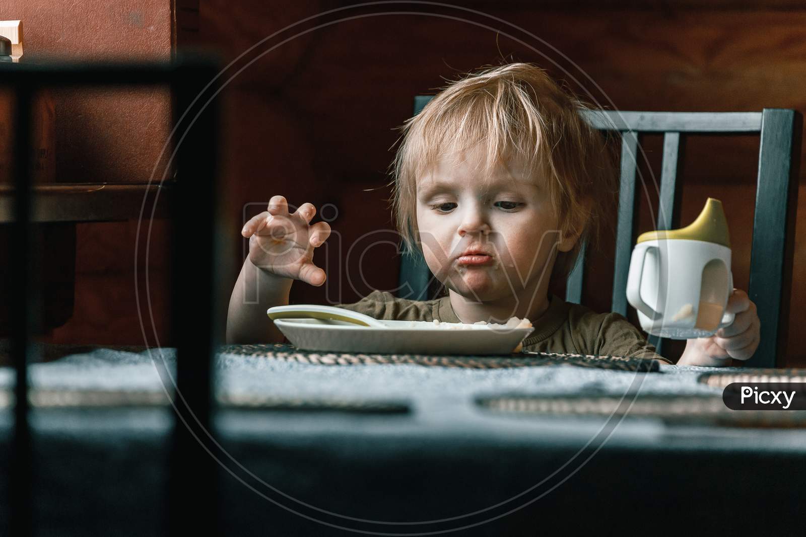 A Toddler Boy On A Chair Holds A Plastic Spoon And Eats His Lunch. Feeding Process. An Infant Child Learns To Eat. Baby Food, Family, Child, Food