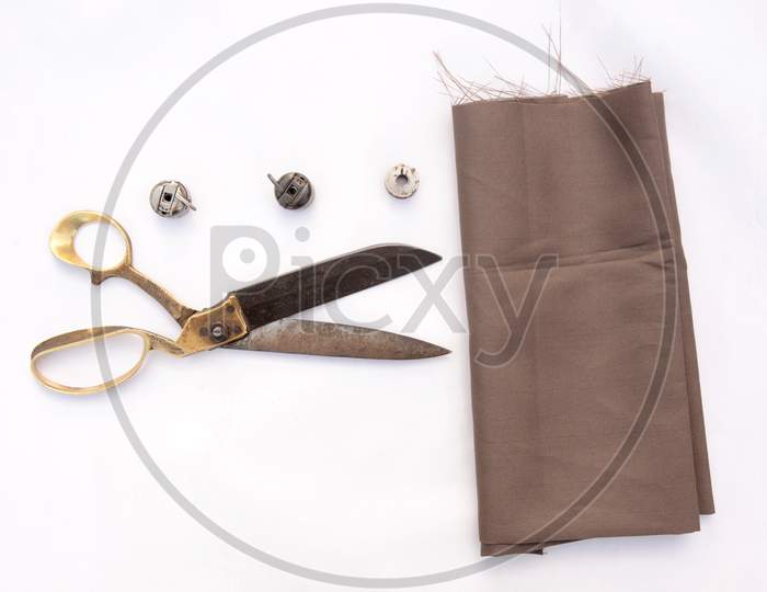 Metal Brass Scissor With Metal Bobbins And Brown Cloth Isolated On White Background.