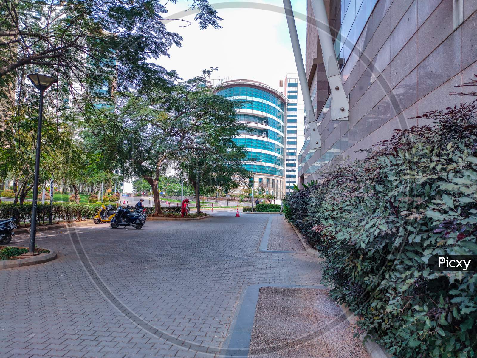 Bangalore, Karnataka, India- December 15Th 2019; Stock Photo Of A Building Or Architecture Of Multinational Company With Blue Glass Window On It , Bikes Parked At Parking Area In Front Of Building In The Afternoon Under Bright Sunlight.