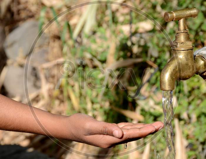 The White Tap Water With Hand Concept World Water Day Over Out Focus Green Brown Background.