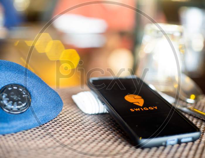 Blue Cloth Mask With Mobile Phone At Side With A Swiggy Logo In Restaurant Showing The Popularity Fo Safe Eating Out And Ordering In As Coronavirus Cases Increase In India