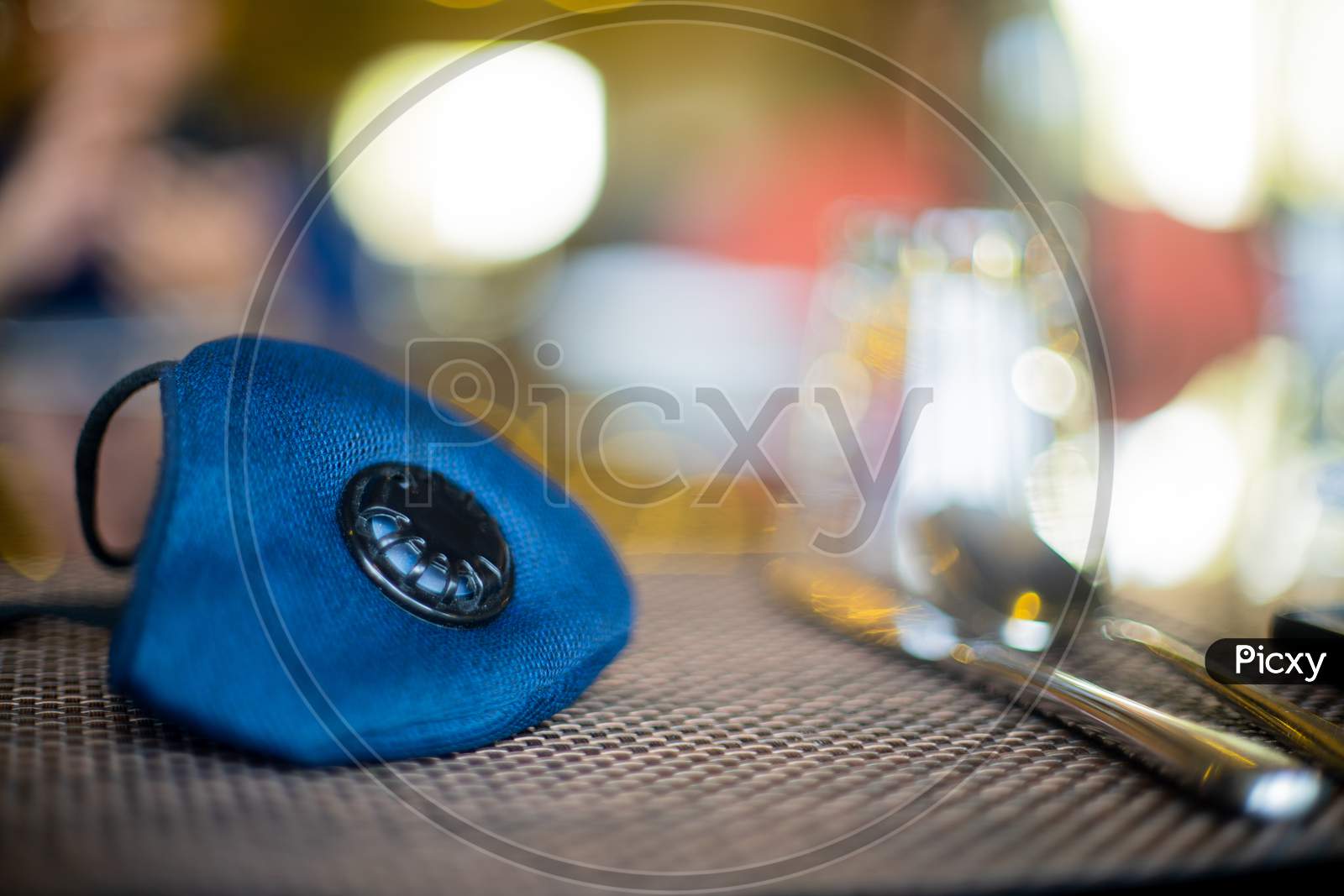 Blue Cloth Mask With Filter Placed On A Restuarant Table With Cutlery Knife And Fork Shot With An Out Of Focus Background