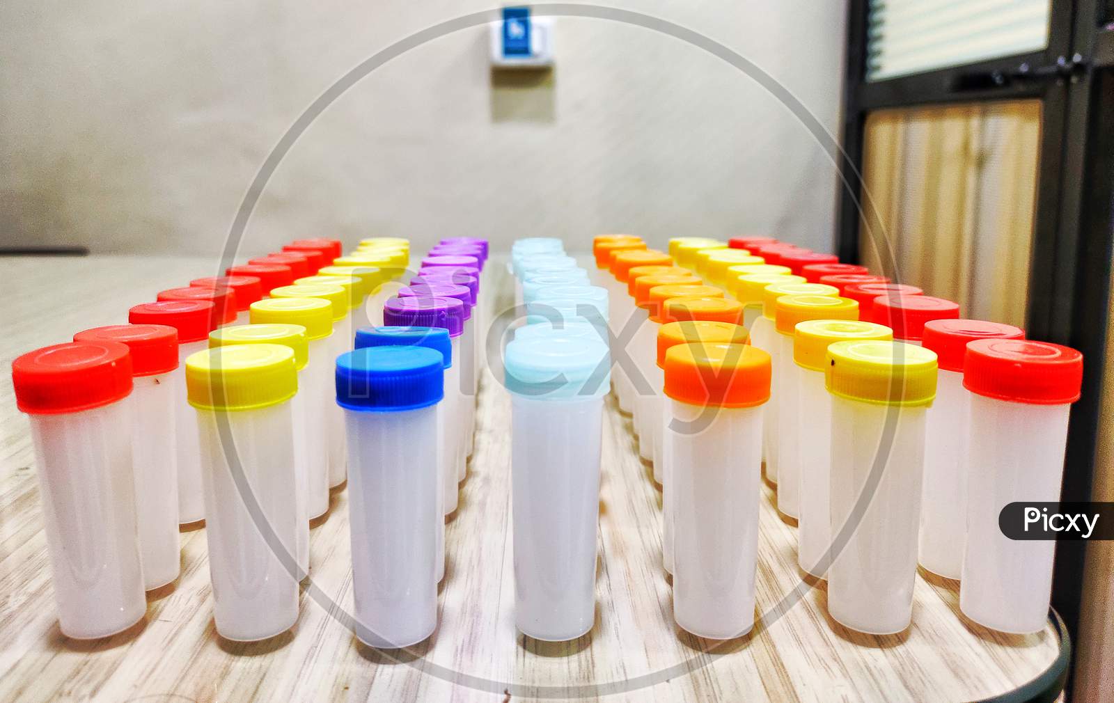 Homoeopathy medicine two drachm plastic bottles with colorful caps lined up in rows on clinic wood table, with blurr background