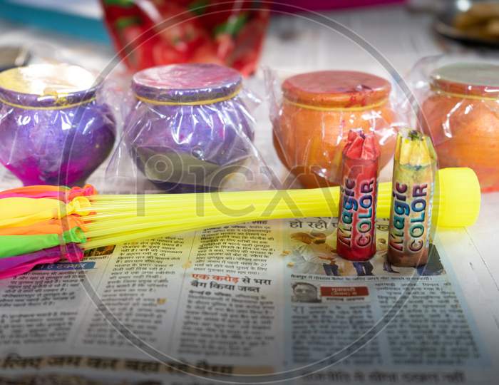 Items To Celebrate Holi Festival Like Colors, Water Balloons, Earthenware Pots With Organic Herbal Colored Powders Kept On A Newspaper In A Shop For Sale