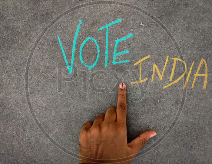 The Inscription Text On The Grey Board, Vote India Using Color Chalk Pieces And Male Hand With Voting Sign Or Inked.