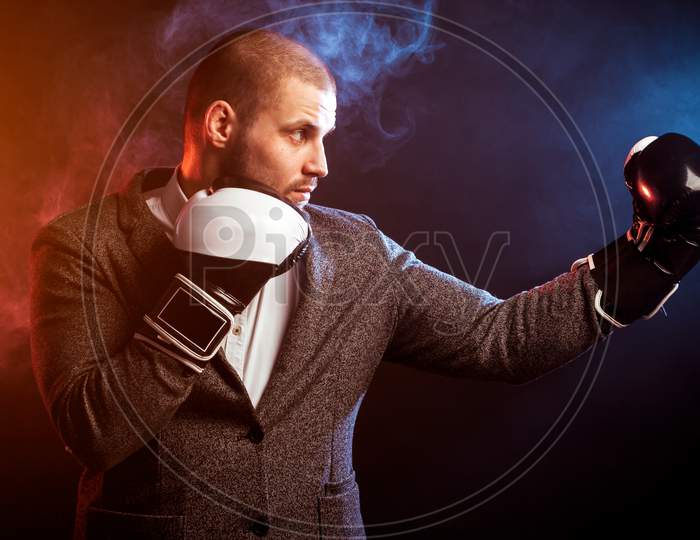 Young Handsome Man Businessman In White Shirt, Gray Suit, White And Black Gloves  Boxing Against Red  And Blue Smoke From A Vape  On Black Isolated
