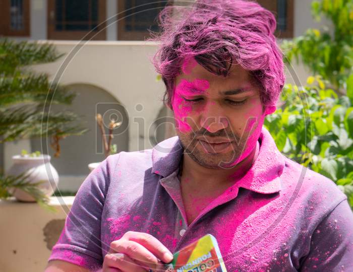 Young Indian Man Covered In Colored Powder Opening A Packet Of Herbal Organic Colors During The Hindu Festival Of Color Holi