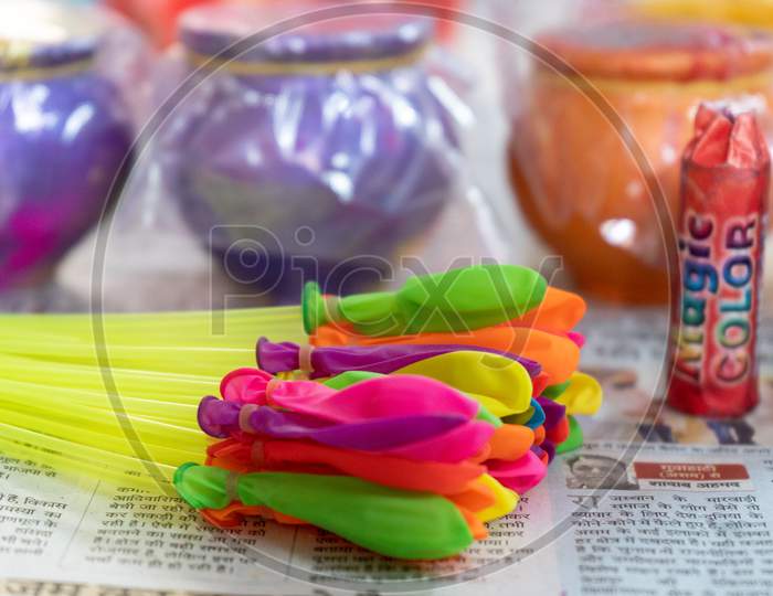 Items To Celebrate Holi Festival Like Colors, Water Balloons, Earthenware Pots With Organic Herbal Colored Powders Kept On A Newspaper In A Shop For Sale