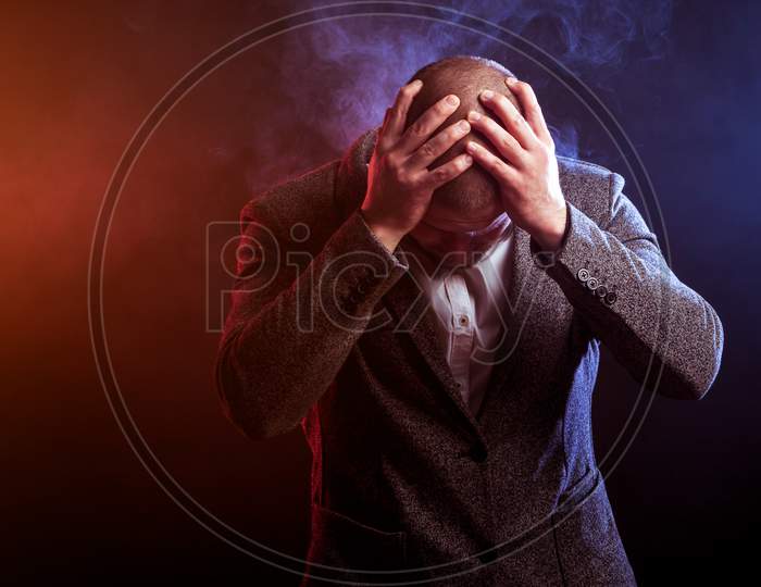 Young Handsome Man Businessman In White Shirt And  Gray Suit  Sad And Took Up His Head  Against Red And Blue Smoke From A Vape  On Black Isolated