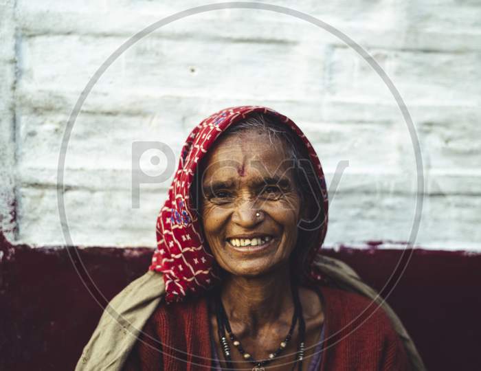 Almora, Uttrakhand - March 2 2021:- Old Aged Woman Sitting With The Support Of The Wall In The Sunset Wearing Indian Traditional Dress And Ancient Jeweleries