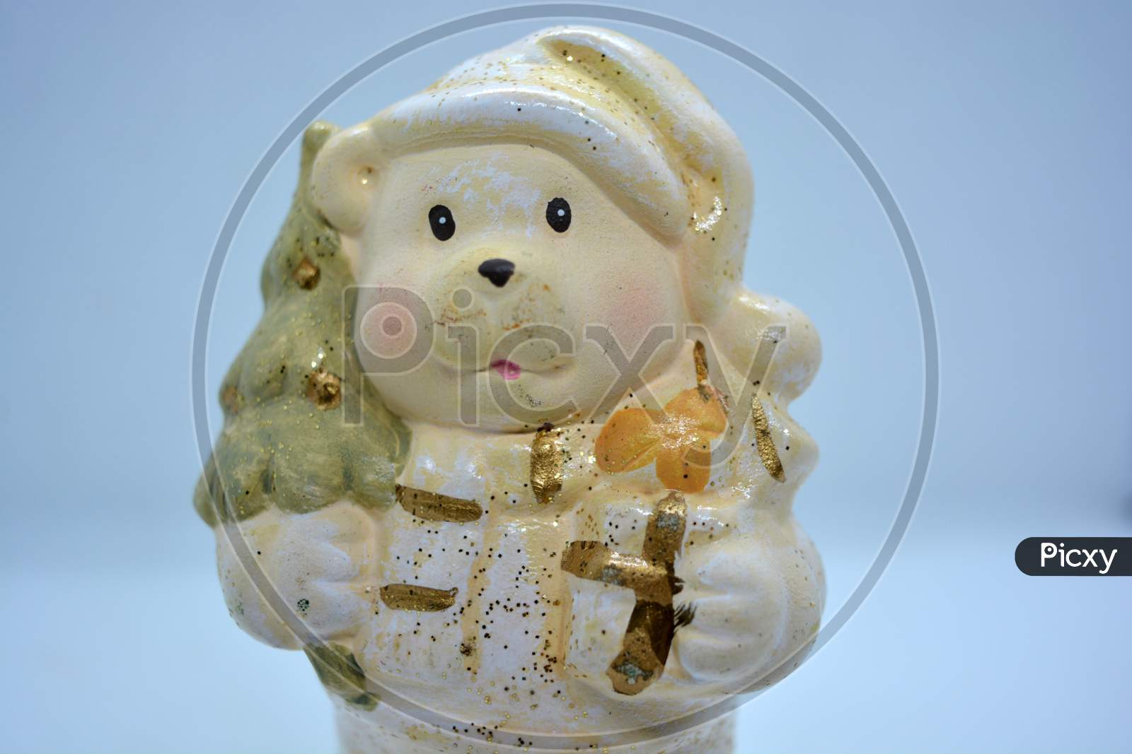 White ceramic statuette of a Christmas teddy bear in a Christmas hat with a golden christmas tree and gifts in hand.