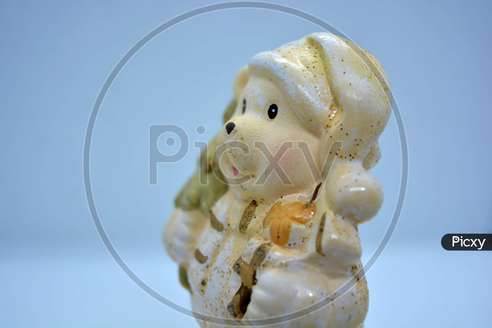 White ceramic statuette of a Christmas teddy bear in a Christmas hat with a golden christmas tree and gifts in hand.