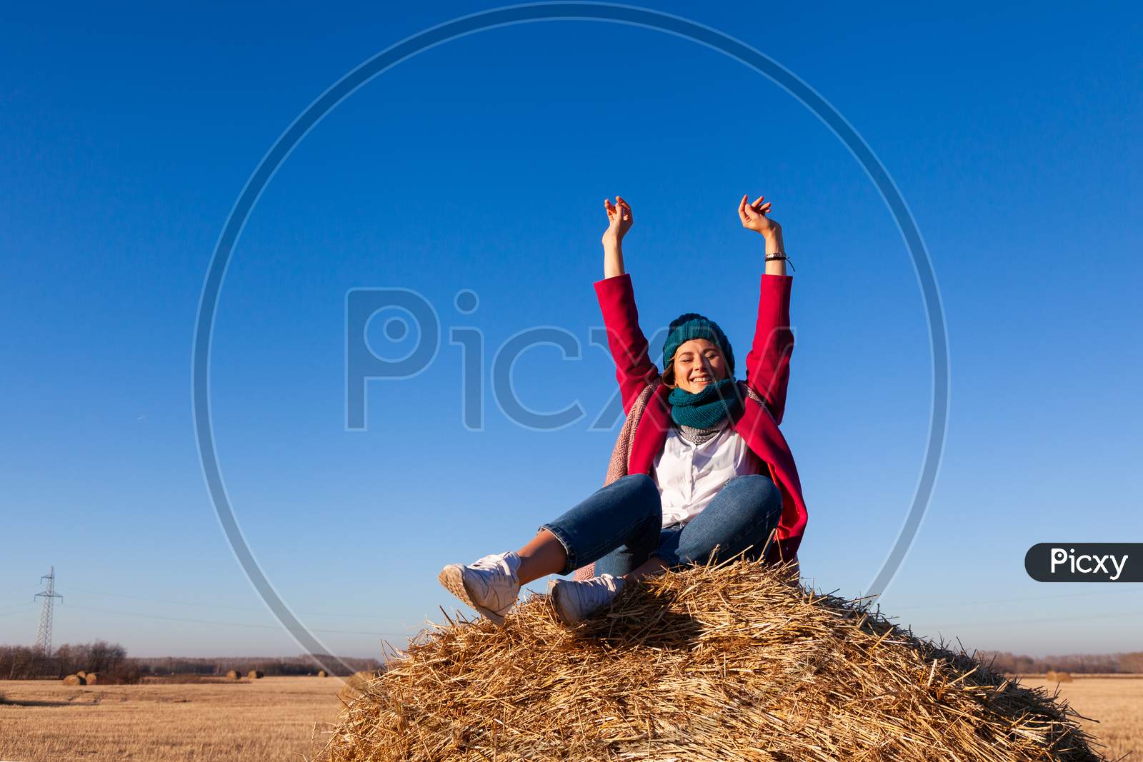 The Concept Of Livestyle  Outdoor In Autumn. Close Up Of A Young Woman Student In A Warm Autumn Clothes Looking Funny, Smilling, Posing For The Camera, Sitting On Haystick