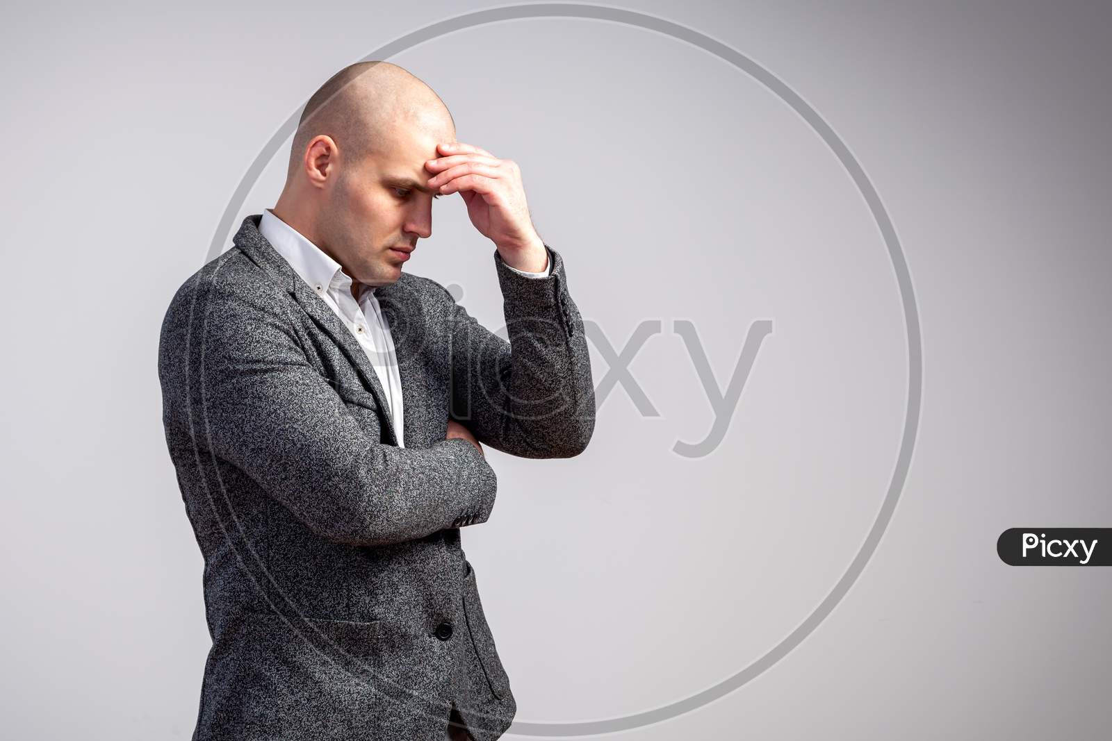 A Young Bald Man In A White Shirt And Gray Suit Is Upset By A Serious Problem In Business, At Work On A White Isolated Background. A Man Has A Headache
