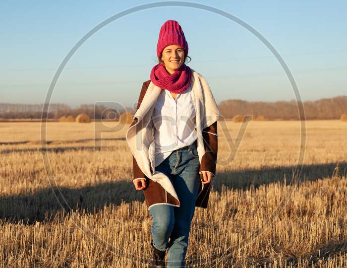Portrait Female Student On Field Background. Beautiful Modern  Young Woman Wearing Pink Knitting Hat  And Pink Coat Smile, Look At The Camera And Enjoy Autumn Sunny Day.