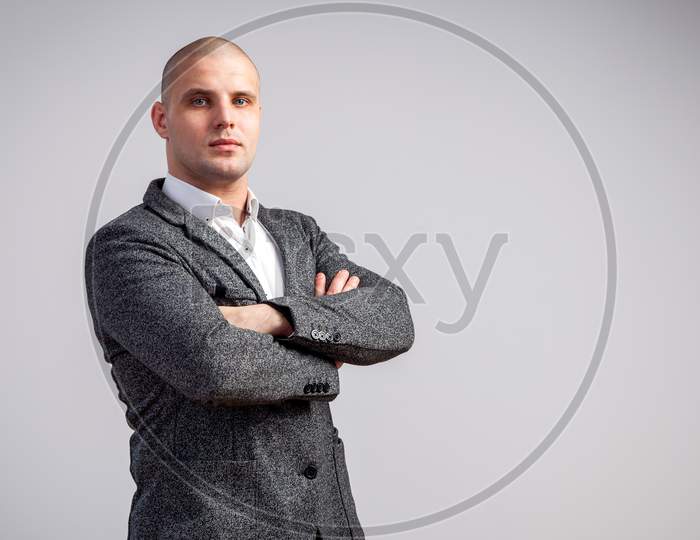 A Young Bald Man In A White Shirt, Gray Suit Confidently Looks At The Camera And Holds His Arms Crossed On His Chest On A White Isolated Background
