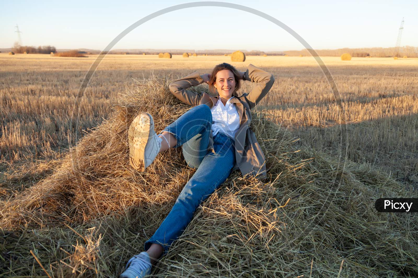 The Concept Of Livestyle  Outdoor In Autumn. Close Up Of A Young Woman Student In A Warm Autumn Clothes Looking Funny, Smilling, Posing, Lying On Haystick Around Field