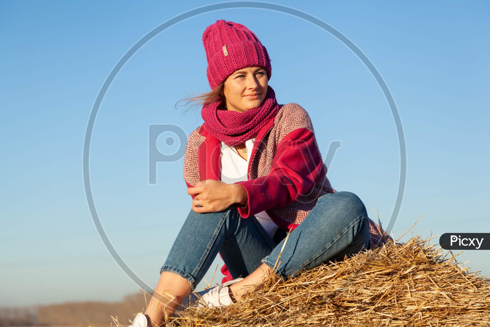 The Concept Of Livestyle  Outdoor In Autumn. Close Up Of A Young Woman Student In A Warm Autumn Clothes Looking Funny, Smilling, Posing For The Camera On  Haystick