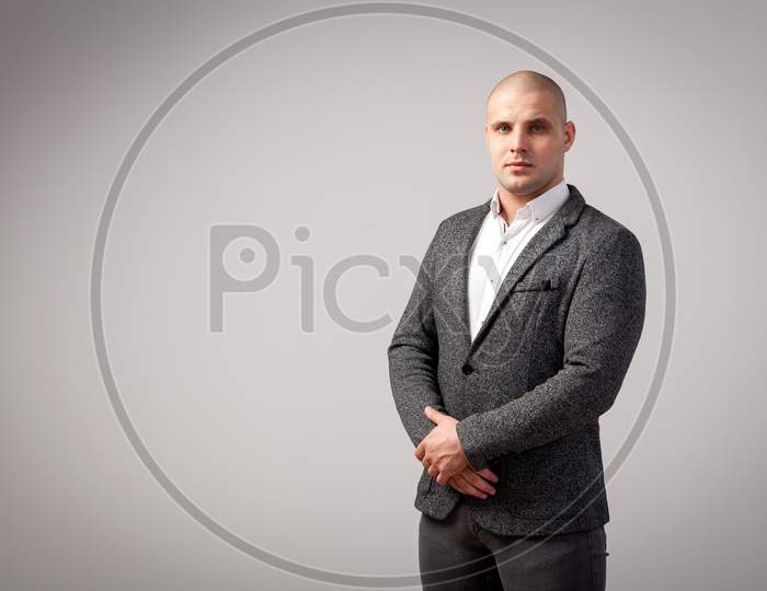 A Young Bald Man In A White Shirt, Gray Suit Strictly Looks At The Camera And Holds His Hands On His Jacket On A White Isolated Background