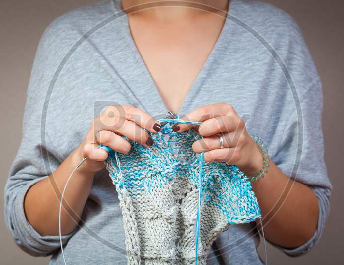 A Close-Up Of A Young Married Woman In A Gray Cardigan Knits With Knitting Needles From Natural Woolen Threads A White And Blue Striped Sweater.
